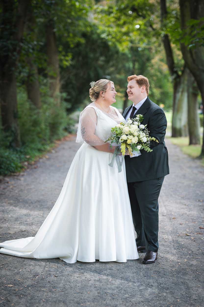 Das Brautpaar steht in einer Allee und schaut sich an